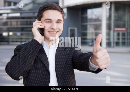 Lachender Manager mit Handy in der Stadt hält seinen Daumen hoch Stockfoto