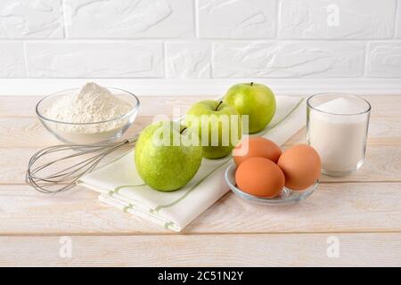 Zutaten für Apfelkuchen: Saure grüne Äpfel, Weizenmehl, Zucker und Eier auf Weißholztisch. Rezept für süße hausgemachte Backen Frühstück Gebäck Stockfoto