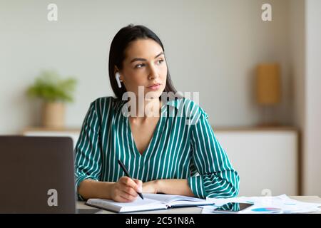Geschäftsfrau Mit Ohrstöpseln, Die Anrufe Entgegennehmen, Notizen Im Büro Sitzend Stockfoto