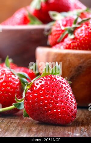 Gesunde Bio Erdbeeren in Holzschüsseln auf dem Holztisch. Frische saftige Erdbeeren im Hintergrund mit einer Erdbeere im Vordergrund. Stockfoto