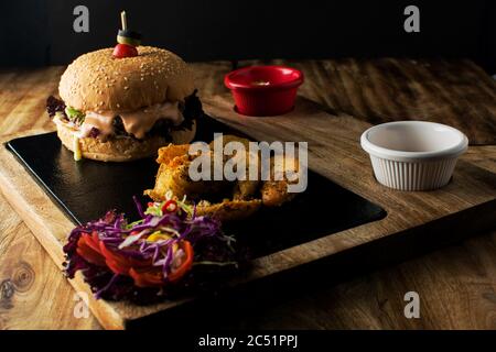 Leckere gegrillte hausgemachte Burger mit Rindfleisch, Tomaten, Käse, Gurke und Salat auf einem dunklen Hintergrund. Draufsicht. Fast Food und Junk-Food-Konzept, lecker Stockfoto