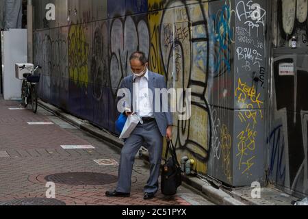 Ein älterer Salaryman überprüft sein Smartphone in einer gepfiffelten Gasse in Shibuya, Tokio, Japan. Stockfoto