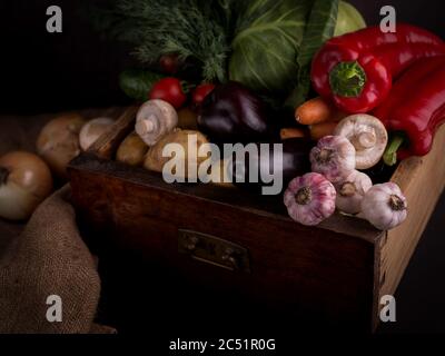 Auswahl an frischem rohem Gemüse in einer Holzkiste vor schwarzem Hintergrund. Gesunde Bio-Lebensmittel aus der Region. Stockfoto