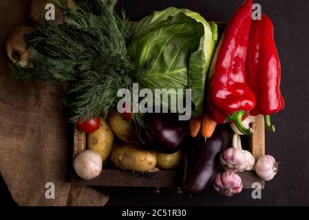 Auswahl an frischem rohem Gemüse in einer Holzkiste vor schwarzem Hintergrund. Gesunde Bio-Lebensmittel aus der Region. Stockfoto