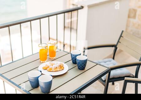 Croissants und frisch gepresster Saft, Gartenmöbel auf dem Balkon mit Blick auf das Meer. Stockfoto