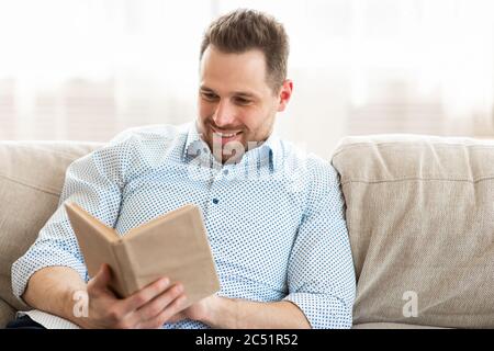 Schöner Kerl, der ein Buch liest, wenn man gemütlich zuhause ist Stockfoto