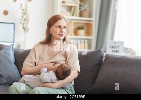 Porträt der reifen Mutter Stillen Baby während auf der Couch im Haus Innenraum sitzen und wegschauen, kopieren Raum Stockfoto