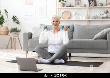 Schulung Zu Hause. Lächelnde Ältere Frau Exzerzisierung Mit Hanteln Vor Dem Laptop Stockfoto