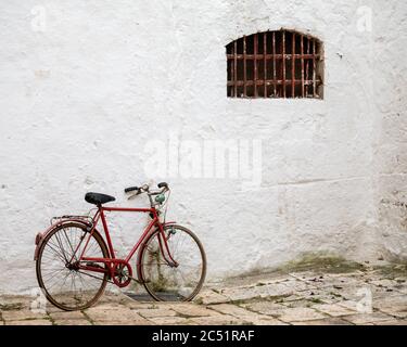 Rotes Fahrrad lehnte sich an ein weißes Gebäude mit einem Fenster Mit rostigen Balustern Stockfoto