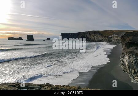 Blick von der Klippe auf Dyrhólaey mit Blick auf schwarzen Lavastrand und Meeresstapel bei Dämmerung im Winter, Island Stockfoto