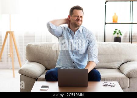 Kerl mit Nackenschmerzen nach langen Stunden bei der Arbeit Stockfoto