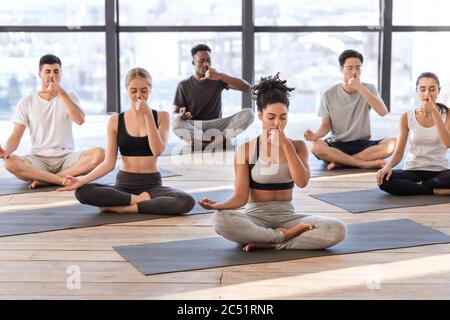 Junge Männer und Frauen im Yoga-Studio üben alternative Nasenatmung Atemübungen Stockfoto