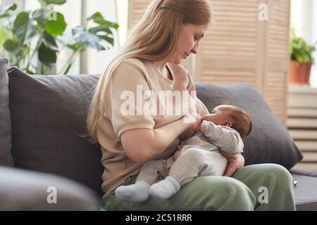 Porträt der ruhigen reifen Mutter Stillen Baby während auf der Couch im Haus Innenraum sitzen, kopieren Raum Stockfoto