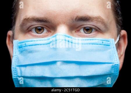 Männliches Porträt eine Nahaufnahme eines Gesichts mit ernstem Ausdruck in einer blauen medizinischen Maske, isoliert auf schwarzem Hintergrund auf einem pneumologistischen medizinischen Thema. Stockfoto