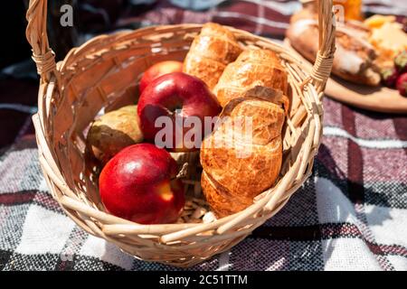 Picknick-Brot, Croissant-Korb mit Obst auf Tuch mit hellem Sonnenlicht. Croissant, Honig, Erdbeere. Gesunde Wahl für die Zeit auf der Natur im Sommer Tag zu verbringen. Essen, Ernährung, gesunde Ernährung. Stockfoto