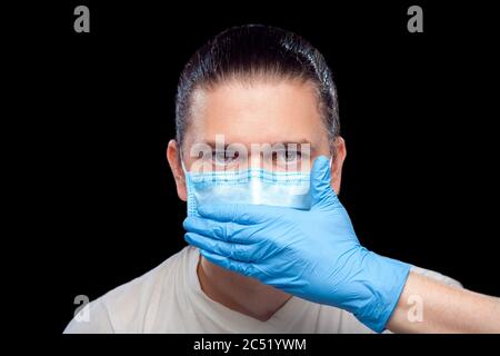 Stumme männliche Porträt Arzt in medizinische Maske und OP-Handschuh decken seinen Mund mit seiner Hand isoliert schwarzen Hintergrund, Konzept stille Protest italienischen s Stockfoto