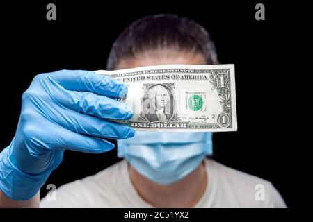 1 Dollar Rechnung in den Händen in medizinischen Handschuhen hält einen Mann in einer kranken Maske, ein Konzept auf dem medizinischen Thema der Kosten der Behandlung und Versicherung Fälle von c Stockfoto