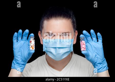 Ein Arzt in einer medizinischen Maske mit sterilen Handschuhen hält in den Händen Optionen für neue Medikamente zur Behandlung von Krankheiten in Glasflaschen gefüllt mit Tab Stockfoto