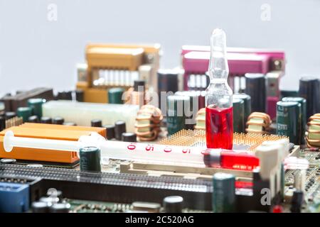 Glasampulle mit rotem Medikament mit Spritze ist auf Sockel mit cpu-Prozessor mit Kontaktbeinen auf dem Motherboard mit mikroelektronischen Komponenten, Nahaufnahme Stockfoto