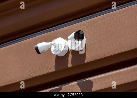 Zwei weiße CCTV-Kameras an der Außenfassade einer braunen Wand, Nahüberwachungssysteme und Fernbedienungskontrolle an sonnigen Tagen. Stockfoto