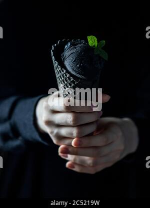 Schwarzes Eis in einem Waffelbecher in weiblichen Händen. Modisches Essen. Speicherplatz kopieren Stockfoto