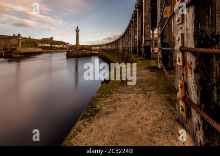 Abenddämmerung am Whitby Hafen vom Ende des Piers. Blick zurück entlang alter Stahlseile in den Hafen Stockfoto