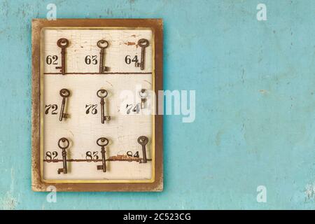 Kleiner Vintage-Schrank mit verrosteten Hotelschlüsseln und Zimmernummern auf blauem erodiertem Hintergrund Stockfoto