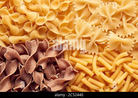 Haufen von verschiedenen rohen Nudeln. Vollkornweizen-Tagliatella; Tubini oder Ziti rigati und Farfalle. Ansicht von oben. Stockfoto