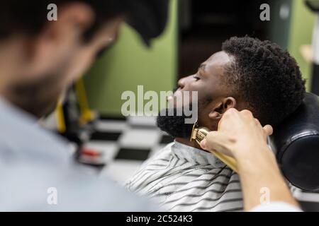 Friseur trimmen Haare mit Haarschneider auf jungen unrasierten schwarzen Mann in Friseursalon Studio.Professional Friseur schneiden Haare mit elektrischen Shearer Maschine auf Afrika Stockfoto