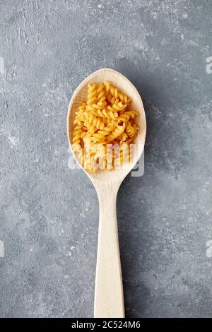 Rohe Fusulli oder Rotini Pasta in einem Holzlöffel auf texturiertem grauen Hintergrund. Overhead-Ansicht mit Kopierbereich. Stockfoto