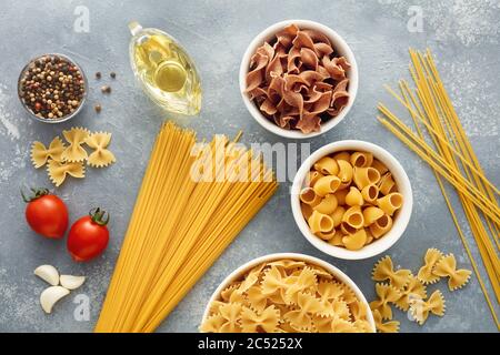 Vielfalt an rohen Nudeln in verschiedenen Arten und Formen mit Tomaten, Öl, Knoblauch und Mehl. Ansicht von oben. Stockfoto