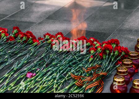 Nelken auf einer Marmorplatte mit einer Spiegelung der Feuerflamme. Symbol der Trauer, Blumenauflegung an der Gedenkstätte. Stockfoto