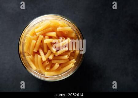 Ziti rigati oder Tubini Pasta in einem Glas auf schwarzem Hintergrund mit Kopierraum. Ansicht von oben. Stockfoto