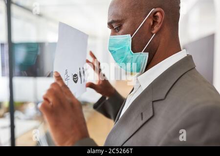 Afrikanischer Geschäftsmann mit Maske wegen Covid-10 fastet Tafel mit Hygienekonzept im Büro Stockfoto