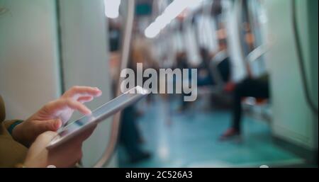 Nahaufnahme einer weiblichen Hand mit Touchpad im U-Bahn-Zug. Andere Passagiere im verschwommenen Hintergrund Stockfoto