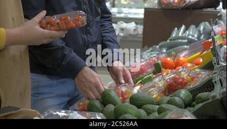 Mann und Frau kaufen Gemüse im Supermarkt. Sie wählen Tomaten in Plastikboxen verpackt. Einkaufen für frische und gesunde Lebensmittel Stockfoto