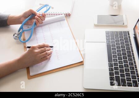 Nahaufnahme der Hände des Arztes, die ein Rezept schreiben und Stethoskop in einem modernen Büro im Krankenhaus halten. Gesundheitswesen und medizinisches Konzept. Stockfoto