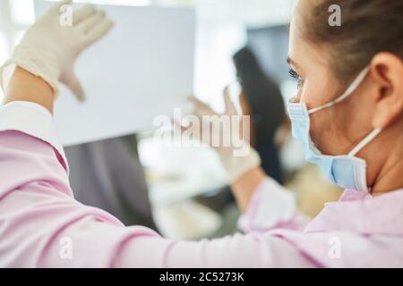 Geschäftsfrau mit Gesichtsmaske befestigt eine Tafel im Büro mit Verhaltensregeln wegen Covid-19 Stockfoto