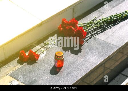 Rote Nelken auf einer Marmorplatte. Die Blumen auf dem Denkmal und die Lampe. Symbol der Trauer. Stockfoto
