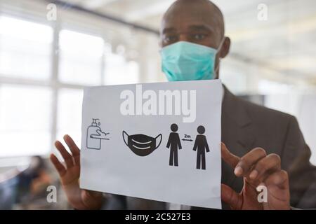 Business-Mann mit Gesichtsmaske wegen Covid-19 befestigt Tafel mit Büro Hygiene-Konzept Stockfoto