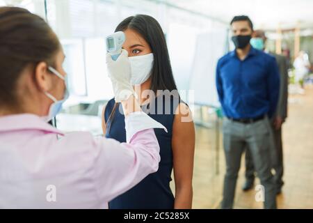 Geschäftsleute mit kontaktlosem Fieber messen ihre Stirn als Prävention gegen Covid-19 im Büro Stockfoto