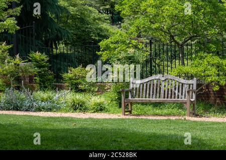 Einsitzige Bank in einem üppigen Sommergarten. Der perfekte Ort, um ein Buch im Freien zu lesen. Stockfoto