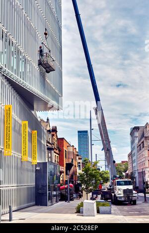 Montreal, Kanada - Juni 2018: Ein Kran und Arbeiter auf einer Aufzugsplattform reinigen die Fenster eines Gebäudes in der Bishop Street in Montreal, Quebec, Kanada. Stockfoto