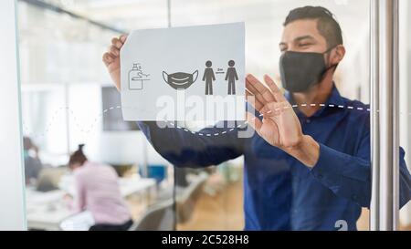 Geschäftsmann mit Gesichtsmaske wegen Covid-19 befestigt Tafel mit Hygienevorschriften im Büro Stockfoto