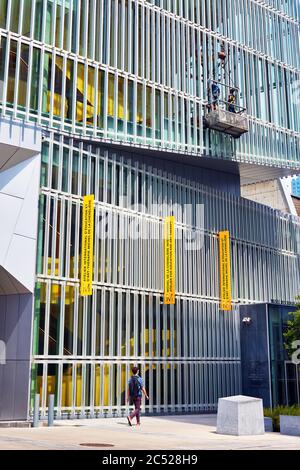 Montreal, Kanada - Juni 2018: Arbeiter auf einer Aufzugsplattform, die die Fenster eines Gebäudes reinigen, während ein Fußgänger auf der Straße in Montreal, Queb, läuft Stockfoto