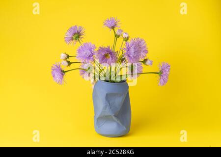 Heller Sommerstrauß von lila Feld Gänseblümchen in einem alten blauen Glas auf einem gelben Hintergrund. Stockfoto