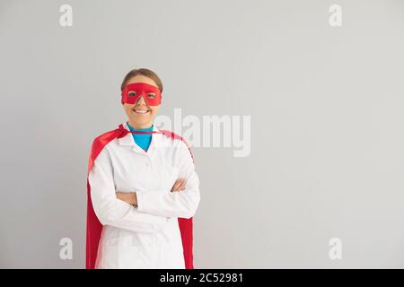 Ein Arzt in einem Superhelden-Kostüm arbeitet in einer Klinik auf grauem Hintergrund. Stockfoto