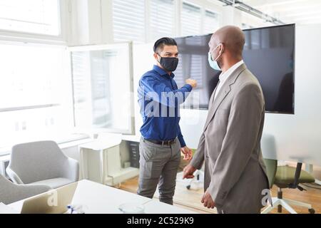 Zwei Geschäftsleute, die eine Maske für Covid-19 und Corona-Virus tragen, diskutieren im Büro über ein Projekt Stockfoto