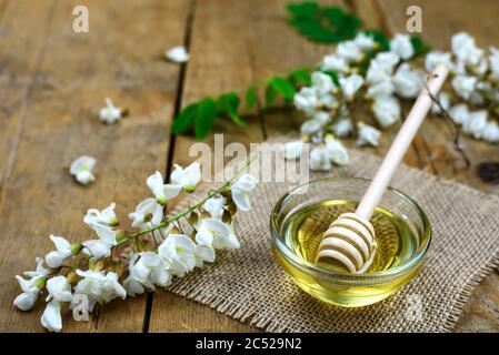Süßer Honig in einer Glasschale mit einem Holzdipper und Akazienblumen auf einem alten Tisch. Selektiver Fokus. Stockfoto