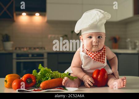 Ein kleines Kind in einem Kochmütze sitzt daneben Gemüse Stockfoto